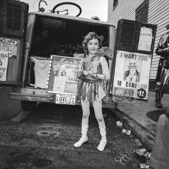 A black and white photograph of a girl standing in front of a truck.