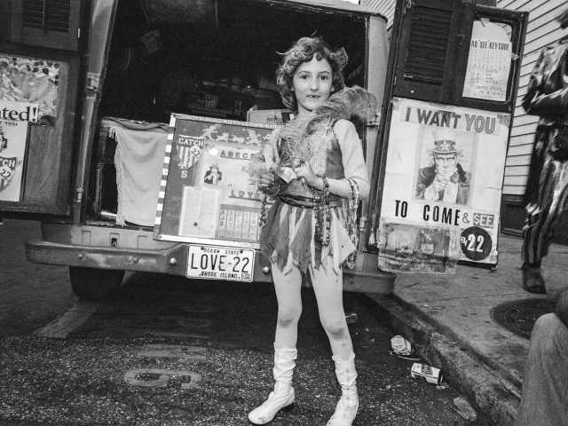 A black and white photograph of a girl standing in front of a truck.