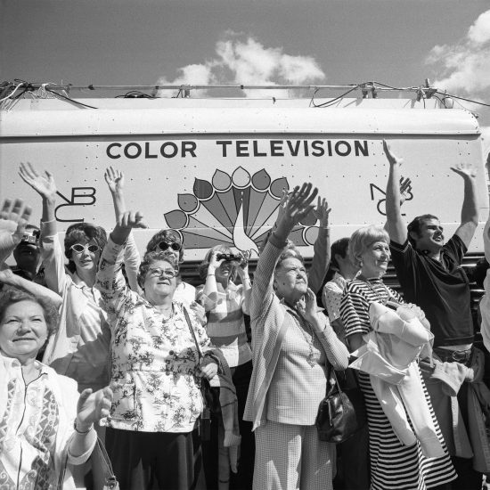 A black and white photograph of a crowd of older women waving to something in the distance at a parade.