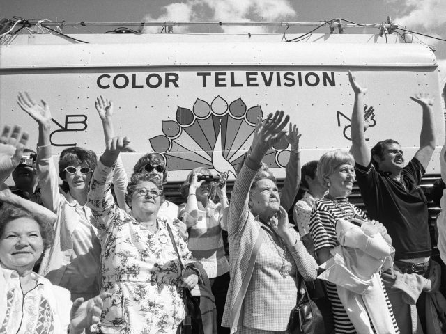 A black and white photograph of a crowd of older women waving to something in the distance at a parade.