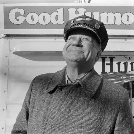 A black and white photograph of a Good Humor salesman staring up at the sky smiling.