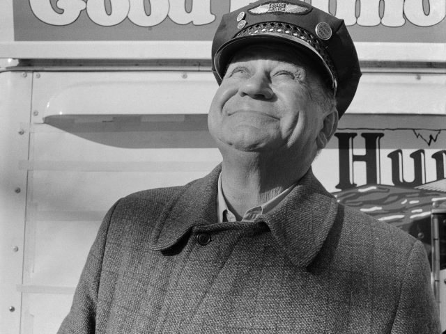 A black and white photograph of a Good Humor salesman staring up at the sky smiling.
