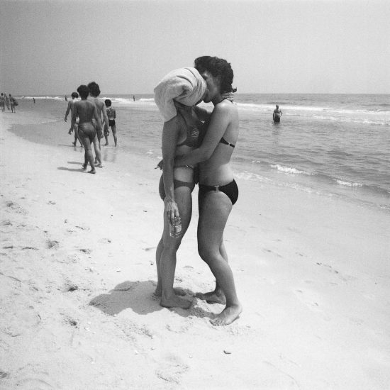 black and white photograph of two women kissing on a beach.