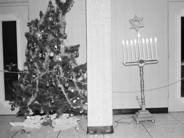 A black and white photograph of a Christmas tree and a menorah in a building's lobby.