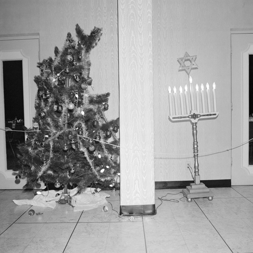 A black and white photograph of a Christmas tree and a menorah in a building's lobby.