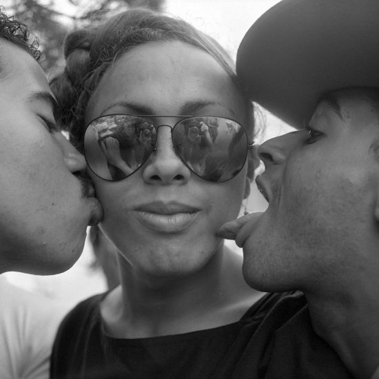 A black and white photograph of a woman being kissed and licked by two men.