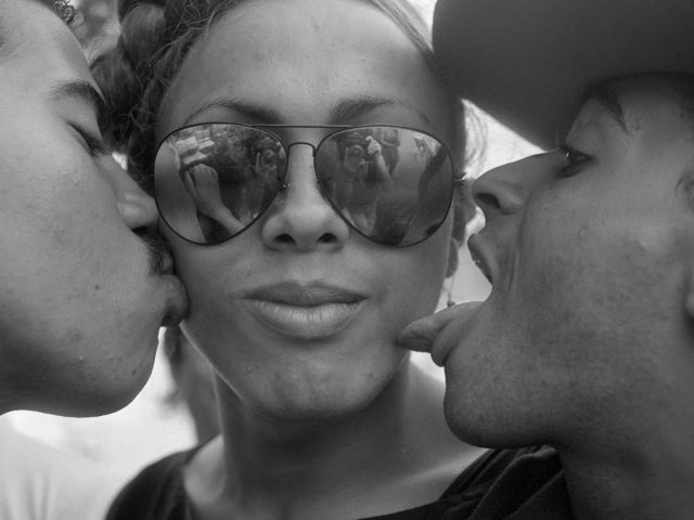 A black and white photograph of a woman being kissed and licked by two men.