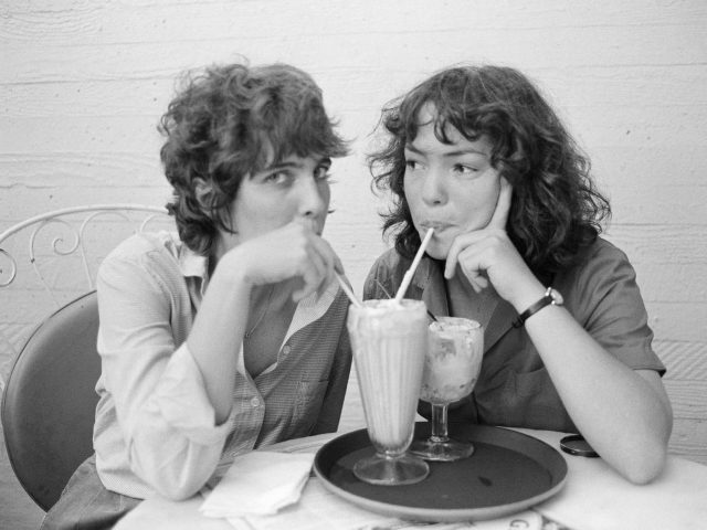 A black and white photograph of two young women sharing a milkshake.
