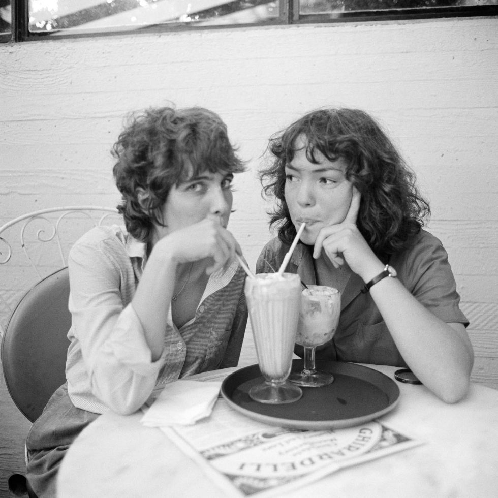 A black and white photograph of two young women sharing a milkshake.