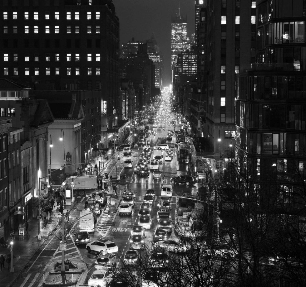 A black and white photograph of a traffic jam on a busy city street at night.