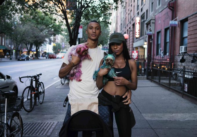 A photograph of a young couple with two dyed small dogs in their arms.