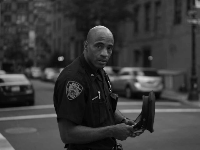 A black and white photograph of a policeman standing in a crosswalk.
