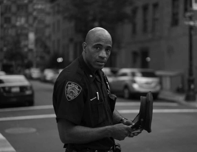 A black and white photograph of a policeman standing in a crosswalk.