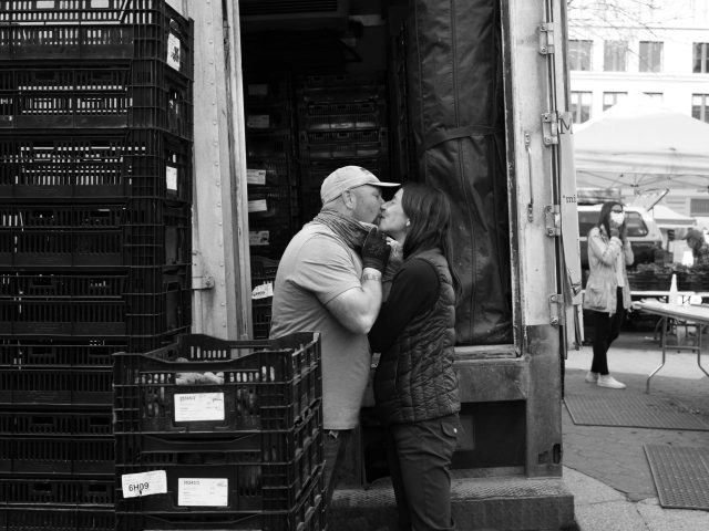 A couple kisses in black and white at the farmer's market.