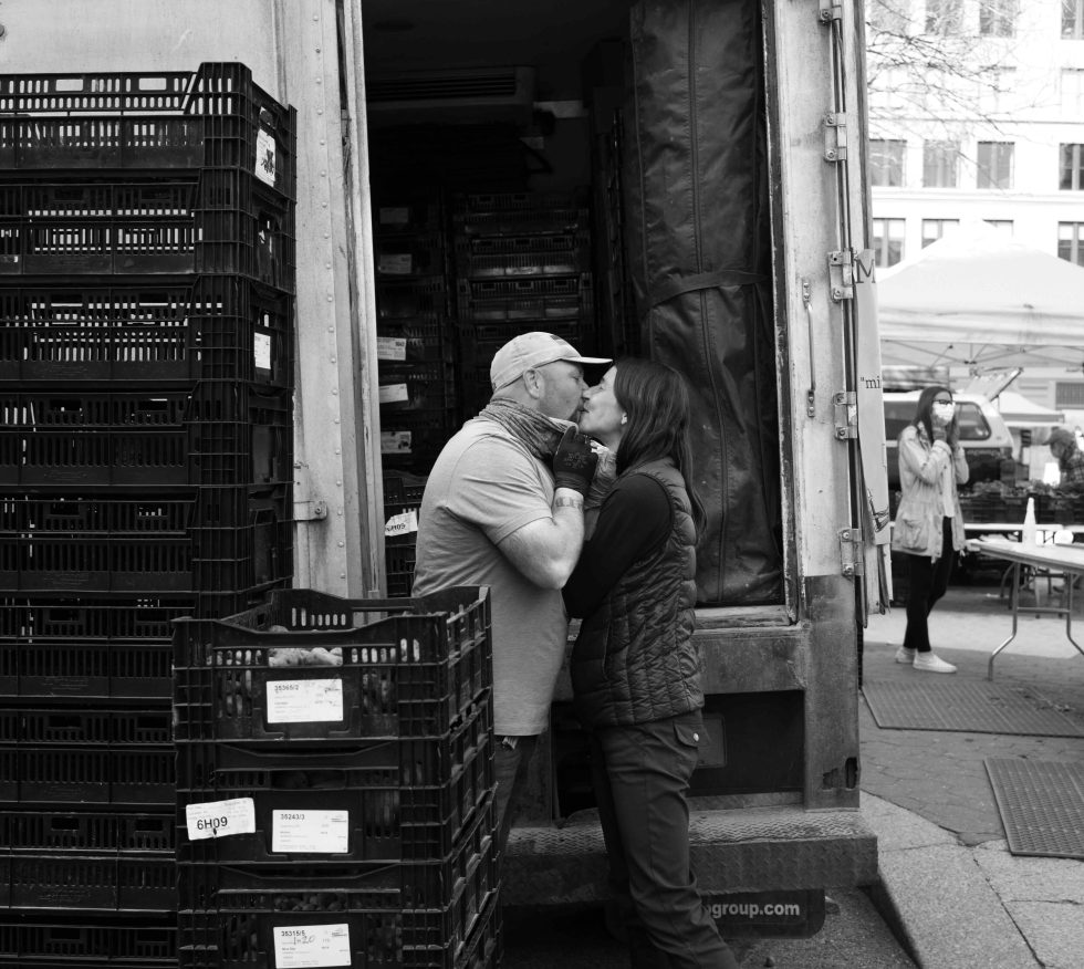 A couple kisses in black and white at the farmer's market.