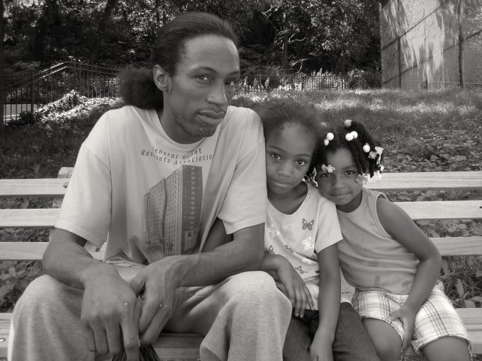 A black and white photograph of a young family sitting on a park bench.
