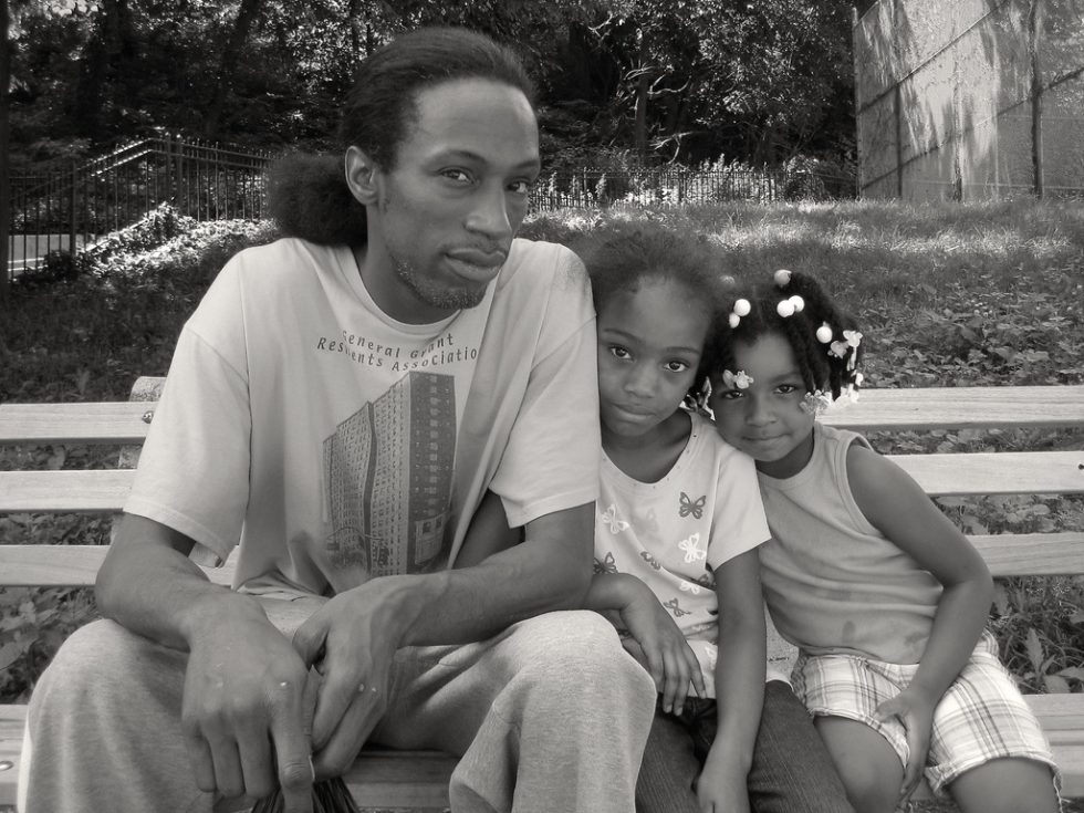A black and white photograph of a young family sitting on a park bench.