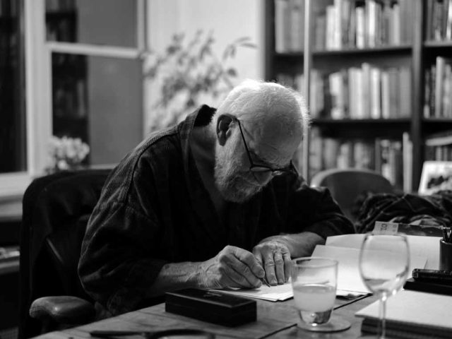 A black and white photograph of an older man working at his desk.