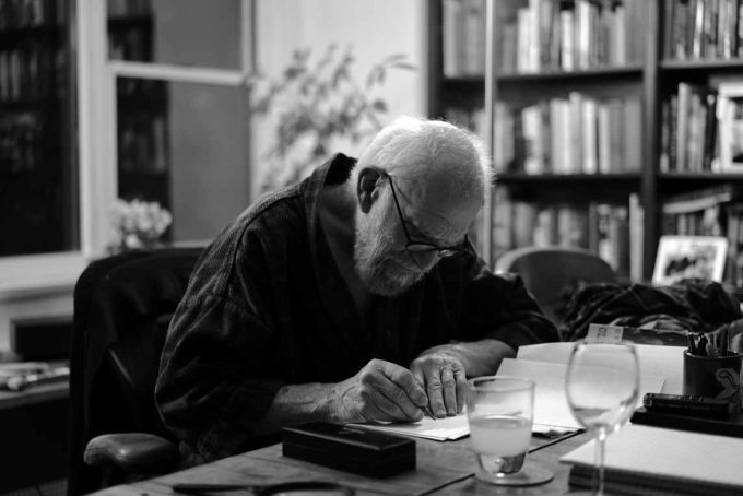 A black and white photograph of an older man working at his desk.