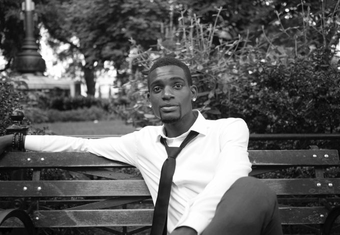 A black and white photograph of a young man on a park bench.