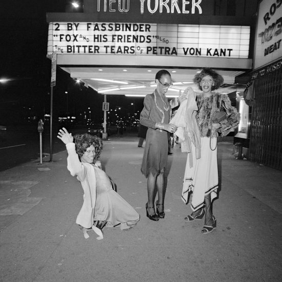 A black and white photograph of 3 people standing below a marquee.