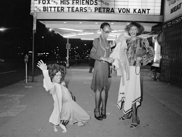 A black and white photograph of 3 people standing below a marquee.