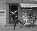 A black and white photograph of a man walking down the street blowing a trumpet.