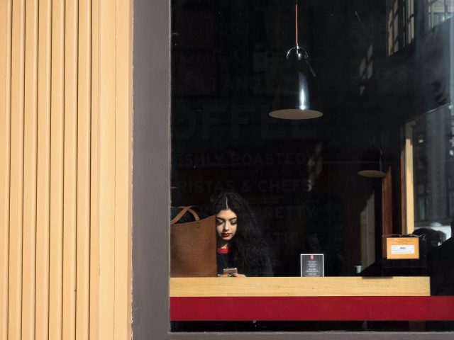 A color photograph of a woman sitting in a coffee shop window wearing lipstick.