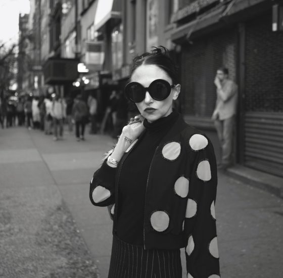 A black and white photograph of a young mother in sunglasses wearing a polka dot sweater.