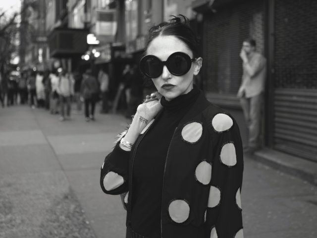 A black and white photograph of a young mother in sunglasses wearing a polka dot sweater.