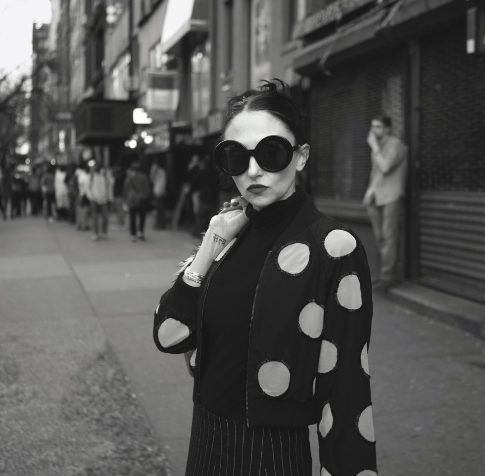 A black and white photograph of a young mother in sunglasses wearing a polka dot sweater.