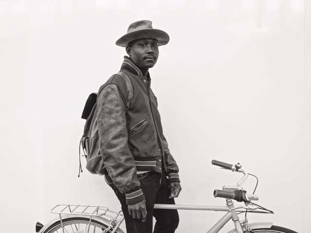 A black and white photograph of a man on a bicycle.