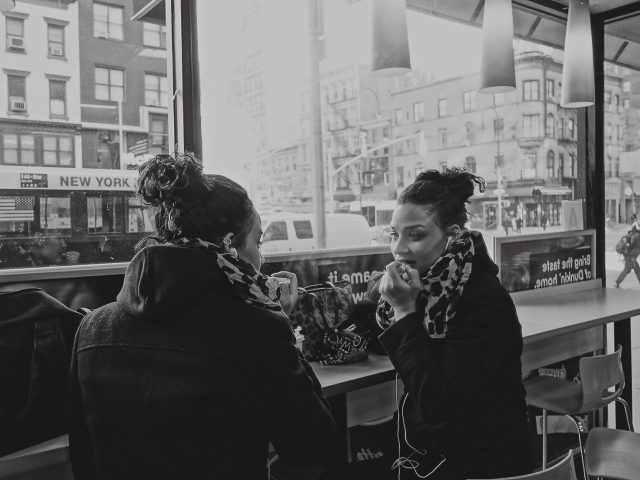 A black and white image of a woman doing her makeup in a mirror at Dunkin'