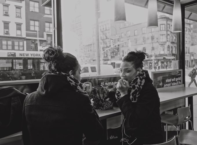A black and white image of a woman doing her makeup in a mirror at Dunkin'