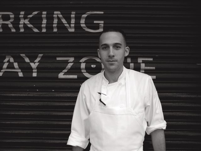 A black and white photograph of a cook having a cigarette outside.