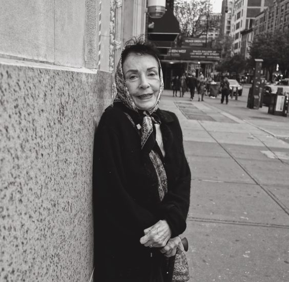 A black and white photograph of an older woman on a city street.