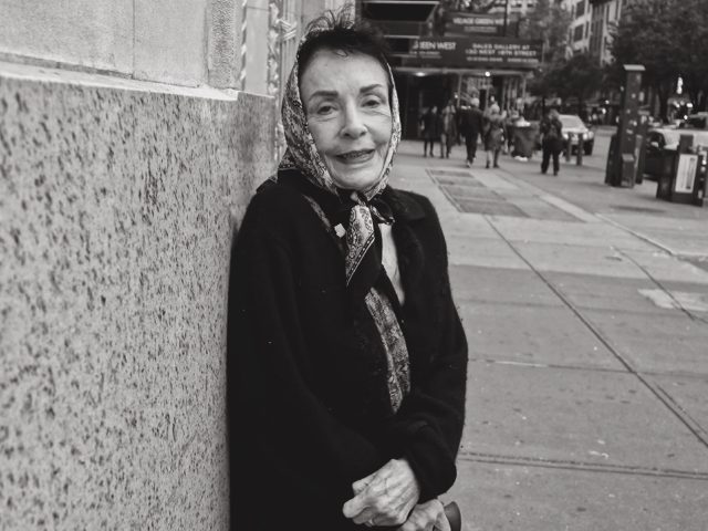 A black and white photograph of an older woman on a city street.