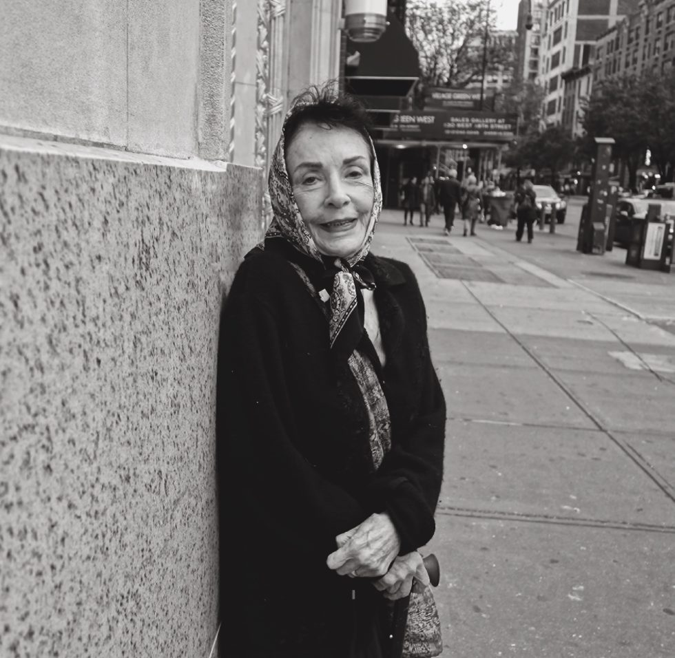 A black and white photograph of an older woman on a city street.