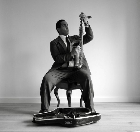 A black and white photograph of a man in a suit setting up his saxophone.