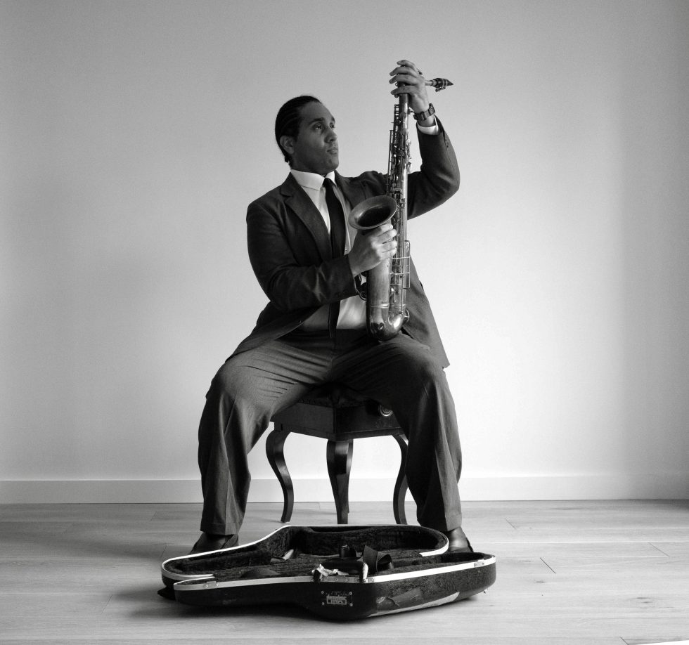 A black and white photograph of a man in a suit setting up his saxophone.