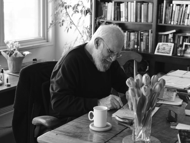 A black and white photograph of an older man sitting at a table at home.