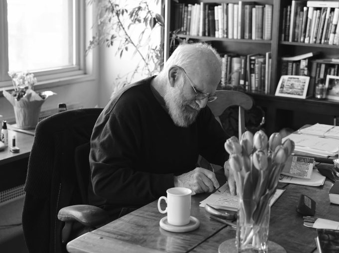 A black and white photograph of an older man sitting at a table at home.