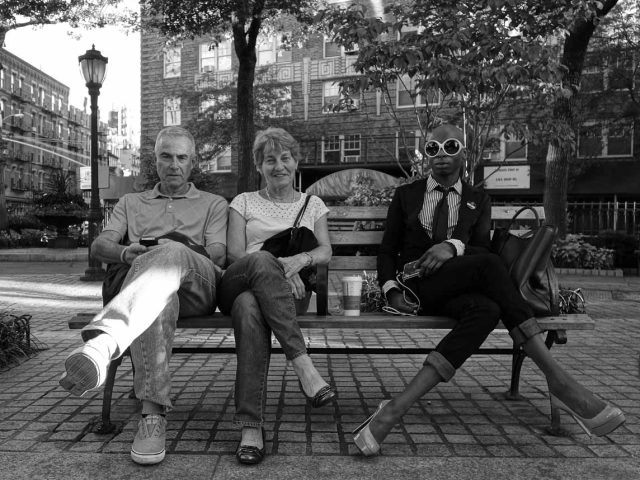 A black and white photograph of a group of people sitting on a park bench.