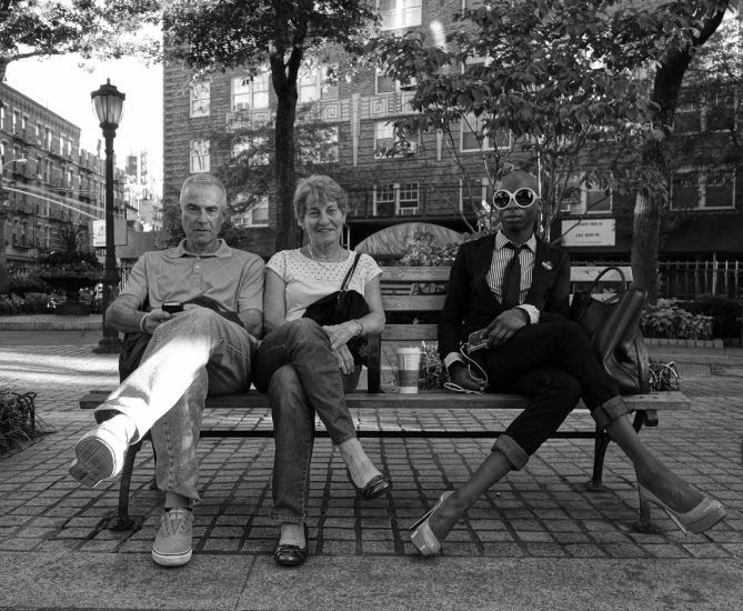 A black and white photograph of a group of people sitting on a park bench.