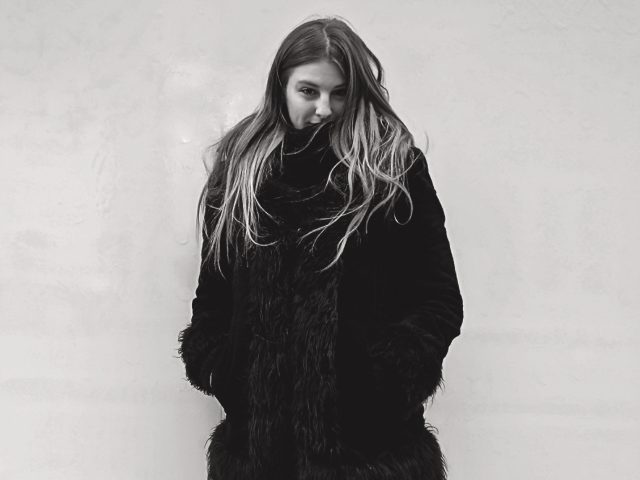 A black and white photograph of a girl in a fur coat.