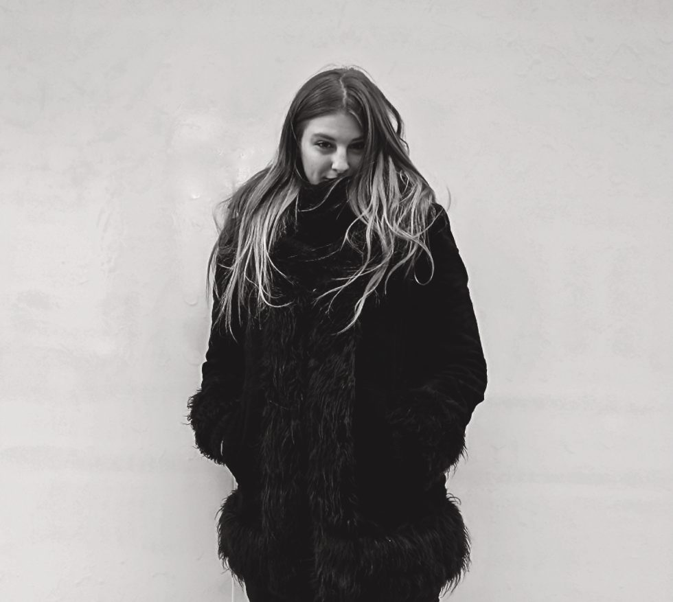A black and white photograph of a girl in a fur coat.