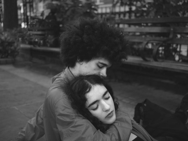 A black and white photograph of a young couple embracing in a park.
