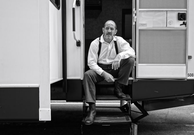A black and white photograph of an older male actor waiting at the entrance of his trailer.