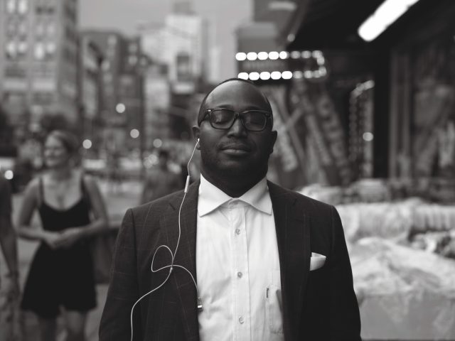 A black and white photograph of a young man, well dressed in a city street.
