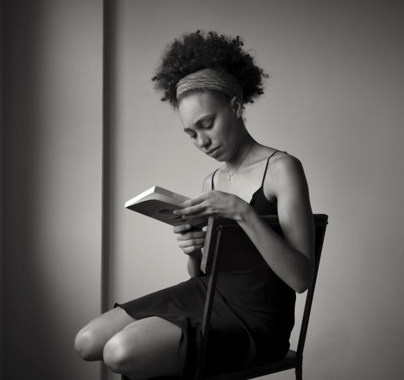 A black and white photograph of a your woman sitting in a chair and reading a book.